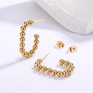 Detailed macro view of golden beaded C-shaped earrings with high-polish 18K gold finish