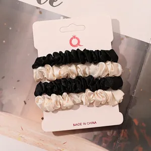 Detailed set of four satin hair scrunchies in black and cream on display card