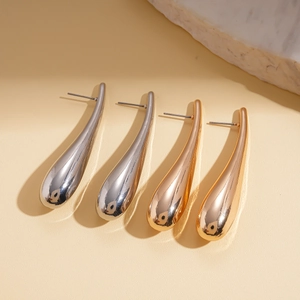 Polished teardrop stud earrings in gold and silver finishes on a textured stone base