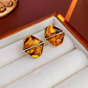 Close-up of geometric amber resin earrings with gold metal frames in a white jewelry box