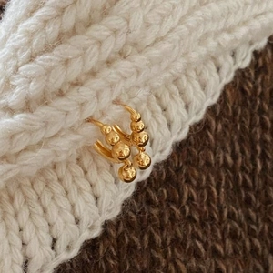 Detailed view of gold hoop earrings with metallic bead charms on a knit texture