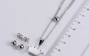 Detailed view of silver crown pendant and ball stud earrings next to a measuring scale