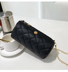Detail view of black quilted cylinder bag with gold floral clasp and chain strap