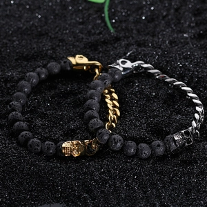 Detail of skull bracelets with lava stone beads and Cuban links on black sand background