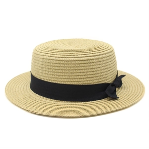 Detail of a brown woven boater hat featuring a flat top and black grosgrain ribbon bow