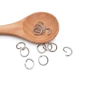 Silver metal jump rings in various sizes displayed on a wooden spoon for DIY crafts