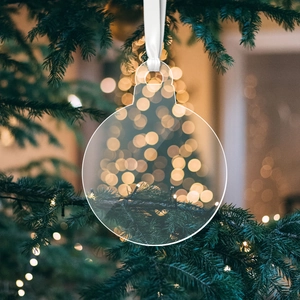 Clear acrylic round Christmas ornament with white ribbon hanging on a blurred festive tree