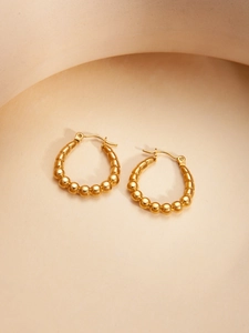 Detailed shot of golden beaded hoop earrings with leverback closure on beige background
