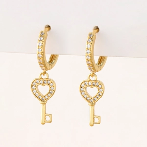 Close-up of gold hoop earrings with sparkling zircon heart key pendants on white card