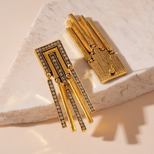 Detailed close-up of golden geometric fringe earrings with rhinestones on a stone stand