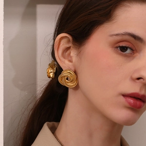 Close-up of a model wearing large 18K gold plated stainless steel twisted knot earrings