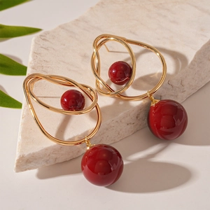 Detail of gold geometric twist earrings with red round beads on a natural stone base