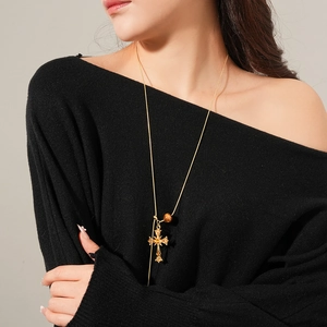 Close-up of model wearing a gold cross pendant necklace with a brown tiger eye bead