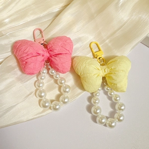 Pink and yellow bow pearl keychains with white bead chains on soft fabric backdrop