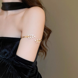 Detailed view of adjustable gold arm cuff with white enamel leaf design on woman arm