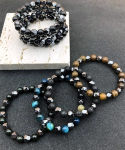 Detail of faceted hematite, tiger eye, and volcanic stone beaded bracelets on stone surface