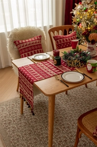 Detailed close-up of red Christmas table runner with reindeer motifs and tassel edges