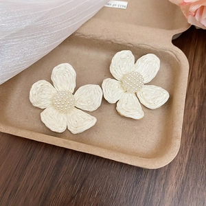 Detail shot of handwoven raffia flower earrings with beaded center in cream white