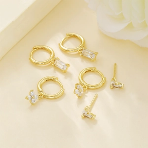 Golden earrings set with cubic zirconia pendants and floral studs on a beige background