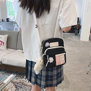 Détail du sac bandoulière en toile noire avec broderie de dessin animé et pendentif d'ours