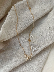 Close-up of gold and silver bow pendants with micro-pave diamonds on a linen background