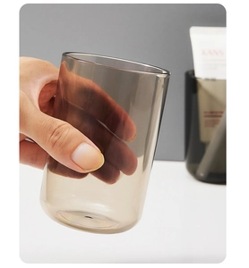 Close-up of hand holding a smoke grey translucent toothbrush cup in a modern bathroom
