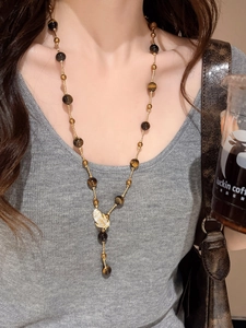 Macro detail of tiger eye bead necklace with rhinestone butterfly pendant on sweater
