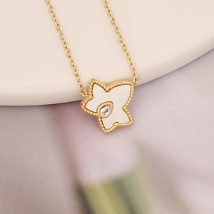 Detailed close-up of golden clover necklace pendant with white shell and droplet crystal
