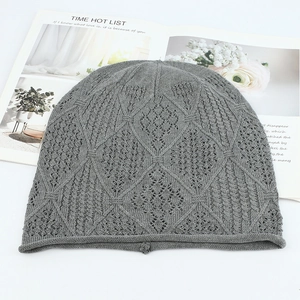 Close-up of grey knit beanie with intricate hollow diamond pattern on a white table