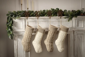 Four knit Christmas stockings in ivory and khaki hanging on a festive fireplace mantel
