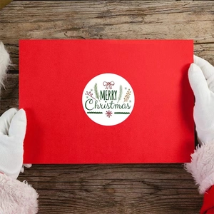 Santa Claus holding a Merry Christmas round sticker on a red card over wood background