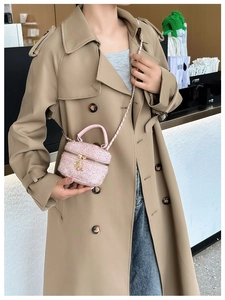 Detailed view of pink tweed mini bag with chain strap held over a trench coat