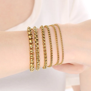 Detail showing 6 gold box chain bracelets in various widths on a person's wrist
