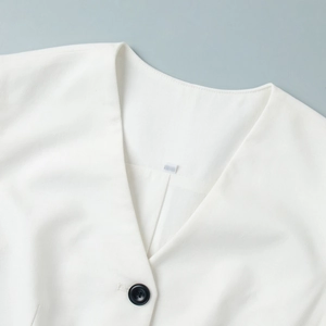 Detail of white V-neck vest collar with a single black button and smooth texture