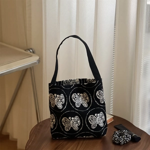 Close-up of white butterfly embroidery and metal magnetic closure on black canvas tote
