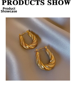 Close-up of golden twisted U-shaped earrings with polished and textured finish on silk