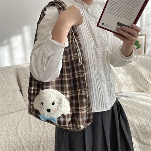 Detail of cute plush puppy on brown checkered tote bag with blue bow accessory