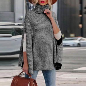Maglione a poncho grigio con collo alto da donna abbinato a jeans in un ambiente esterno