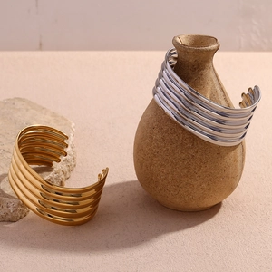 Detail of layered gold and silver wide open cuffs on rustic stone and ceramic bases
