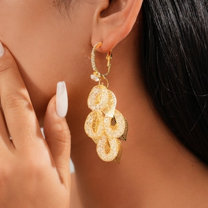 Detail of leaf tassels and mesh rings on a gold earring worn by a model