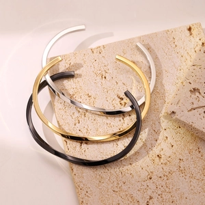 Bracciali rigidi a C minimalisti in oro, argento e nero su sfondo di pietra naturale