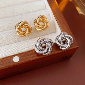 Detailed view of twisted knot stud earrings in gold and silver finishes in a jewelry box