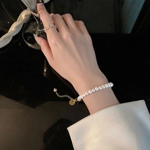 Elegant natural pearl bracelet with gold Fu pendant and ring set on model holding glass