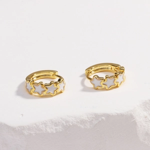Detail view of gold huggie earrings with white enamel star charms on stone