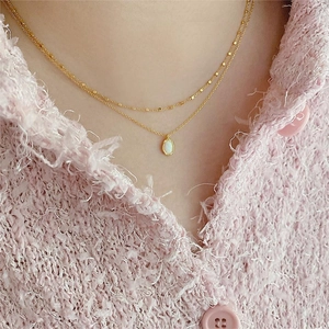 Detail of a gold double-layer necklace with an oval pendant on a tweed jacket