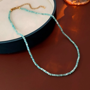 Détail du collier en perles turquoise avec fermoir doré sur un plateau minimaliste