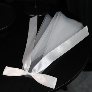 Detailed view of white tulle bridal veil with a glossy satin ribbon bow accent