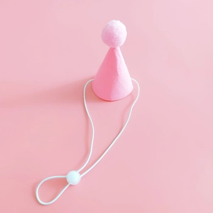 Close-up of pink felt birthday hat for pets with white pompom and adjustable strap