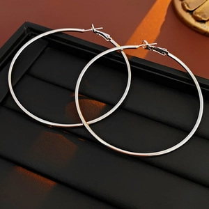 Macro shot of large slim silver circular earrings on black leather stand with warm lighting