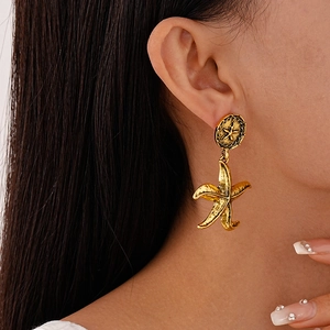 Detail view of retro gold starfish earrings with textured metallic finish on model